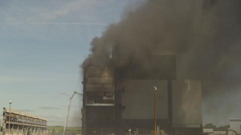 Black smoke billows from tall building, water is spraying from a crane at the building