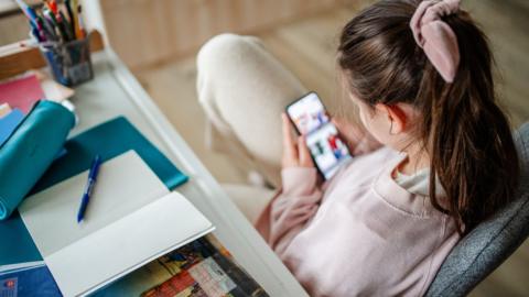 Female student distracted by smartphone while studying at home