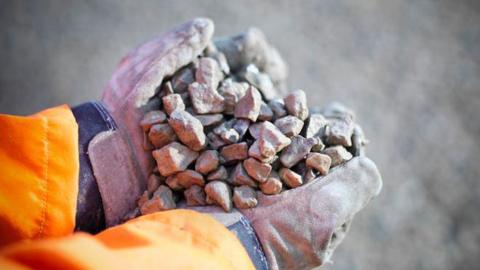 A close up image of a person's gloved hands holding gravel.
