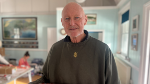 The photo shows David Pond smiling at the camera wearing a green jumper. 