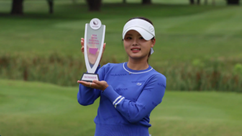 Jessica Bang posing for photographs on a golf course while holding a trophy