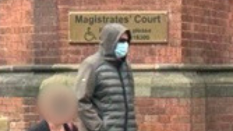 A man who wears a hooded jacket, face mask and sunglasses exits Magistrates' Court