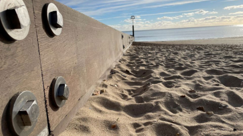 A picture of a beach in Dorset, with a timber groyne to the immediate left of the picture, with the sea in the distance on a fine sunny day.