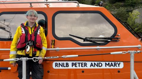 Ellie Nic a' Phearsain na seasamh air bòrd bàta RNLI Phort Rìgh.