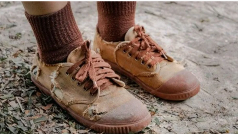 A child wearing a pair of brown shoes which are falling apart 