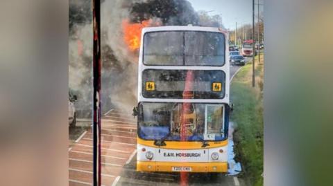 A double decker bus with flames coming out of the side.