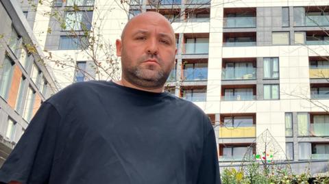 Josh Cope stands in front of Varney Court, a block of flats, with two balconies seen burned