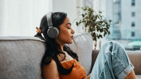 Shot of a young woman using headphones while relaxing on the sofa at home
