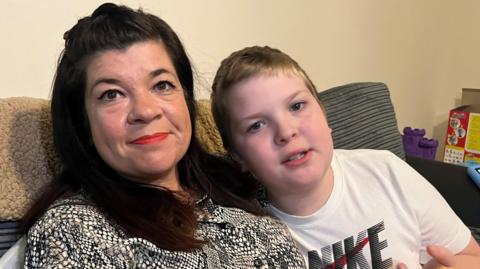 A dark haired lady with her young son in a white t-shirt sitting in their living room