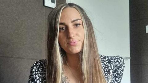 Jade McEnroe is seen wearing a black and white top in front of a brown and white wall.