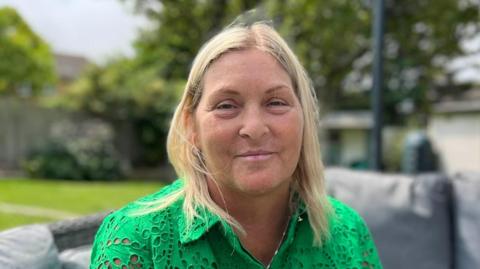 A woman with blonde hair and a green top smiles directly into the camera. 