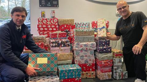 Maksym Litvinov and Andy Evangelou crouch next to a pile of Christmas presents. 