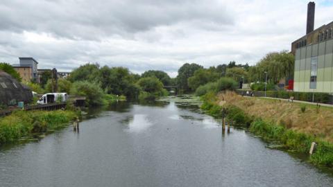 The River Nene upstream of South Bridge, Northampton, showing a factory on the right and some flats in the distance on the left.