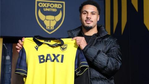 Myles Peart-Harris holds up an Oxford shirt