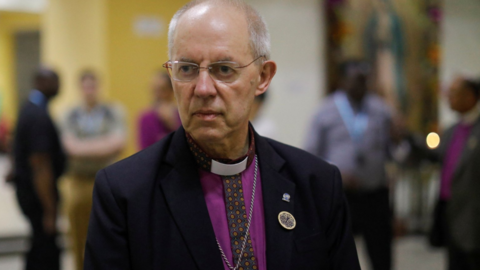 Justin Welby dressed in a purple shirt and dark jacket 