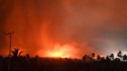 Palm trees and telephone wires are seen beneath an orange sky as Mount Lewotobi Laki-Laki erupts