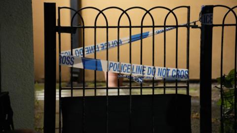 A night time scene showing police tape on a garden gate