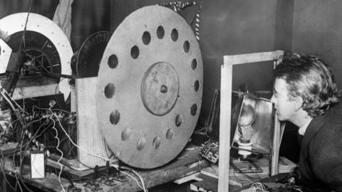 A black and white image of John Logie Baird, the inventor of television, with his transmitting station, transmitting disc.