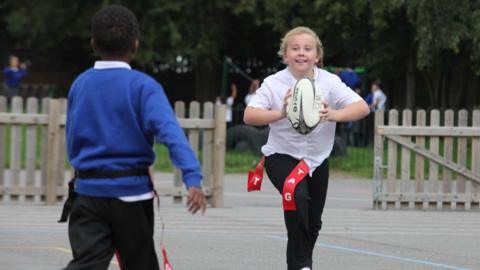 Girl throwing a rugby ball to another pupil.