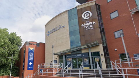University of Wolverhampton buildings which are partly red brick with a stone and glass frontage. A sign in white letters on the right says the Ambika Paul building and a mainly blue sign on the left includes the words sports centre in white letters.