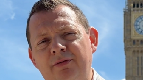 Matt Chorley is wearing a light grey suit with a white shirt. He is stood with the tower of Big Ben behind him.