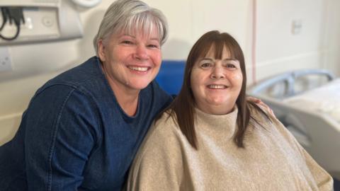 Two women, one with blonde/silver hair, and the other with brown hair posing for a photo in a hospital room