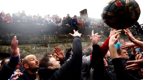 Crowds with hands aloft battling for a huge ball in front of spectators lined along a bridge's parapet