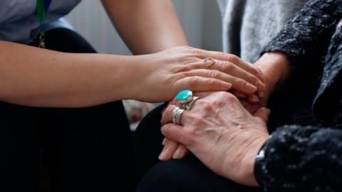 A stock image of a nurse holding the hand of an elderly patient.