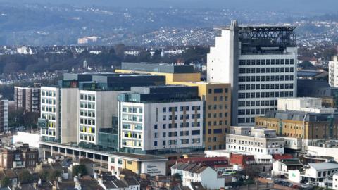 An aerial photograph of a building made of three multi-coloured arms with a tower to the right of it.