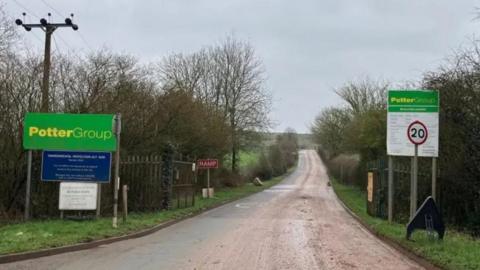 A long drive, with bushes on either side, leading past green signs which read The Potter Group.