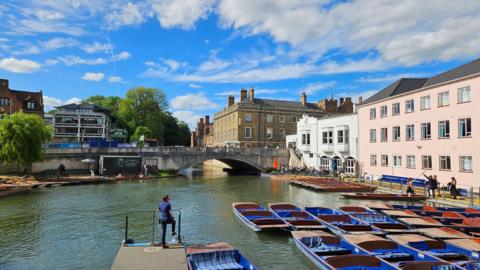Blue sky and cloud over a river partly filled with punting boats in Cambridge