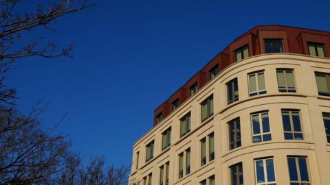 The curved corner of a limestone government building with clean lines set against a clear blue sky.