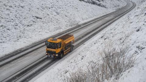 A gritting lorry driving along a snow-covered road.