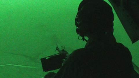 View from rear through a night vision camera of a soldier operating a gun at night from a helicopter in Afghanistan