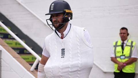 Chris Woakes walking out to bat with his arm in a sling.