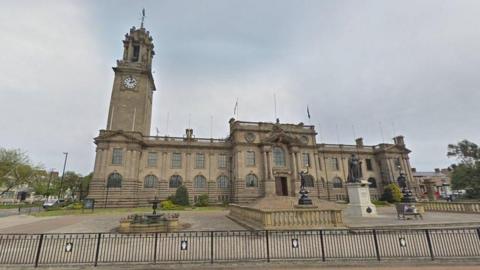 South Tyneside Council headquarters which is a large sandstone building with a clock tower and statues and railings at the front.