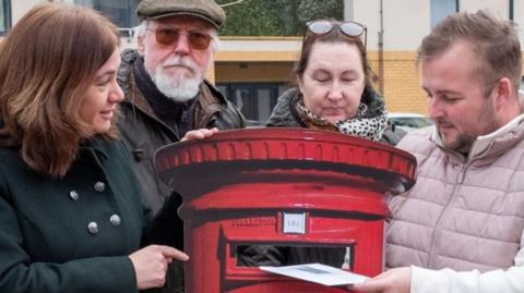 Labour MP Alex Mayer is stood with a group of residents with a cardboard cut out of a post box