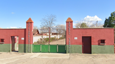 The outside of the Angel Tardio sports centre. A set of iron gates is visible, with two columns on either side and walls painted green and red. The sky is blue in the background.