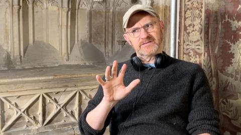 mark gatiss in front of a church wall