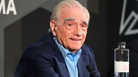 Martin Scorsese in a blue suit with light blue shirt looking at the camera and smiling