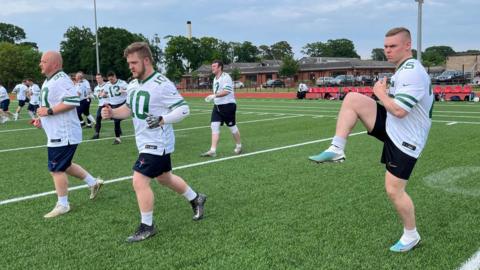 Men in white football strip doing exercises on a football pitch