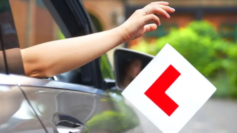 A hand dropping a learner driver sticker out of a car window. 