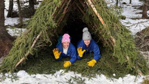 Two people in blue coats are on the ground, both with yellow gloves and their right hand waving at the camera.