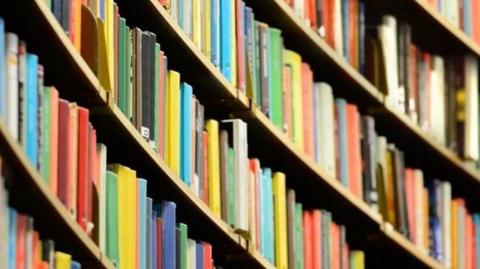 Colourful books line shelves inside a library, with rows of bookcases extending into the distance.