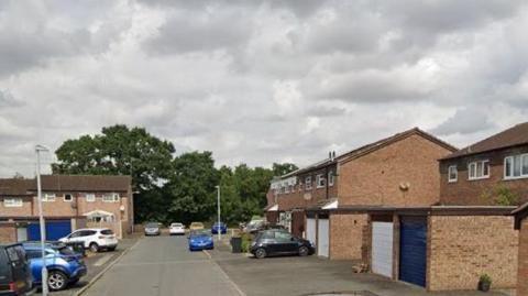 Valley Way, Droitwich. The residential road has several houses with garages and parked cars. At the back of the picture is some trees and some lampposts are also in the photo. 