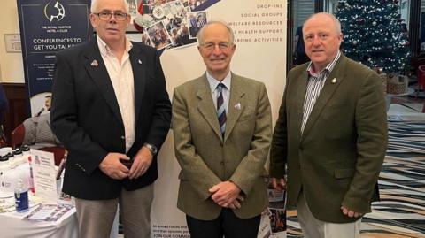 Three men standing in front of banners at an event. 