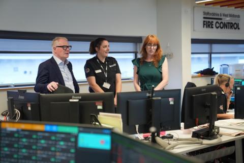 Three people in a fire service control room overlooking computers on desks.