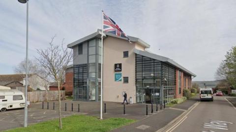 A view of the outside of Williton Library on an overcast day with a caravan in the nearby car park.