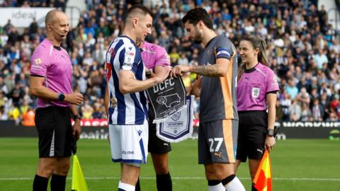 West Brom's Jed Wallace on the left and Derby County's Lewis Travis exchange club's pennants