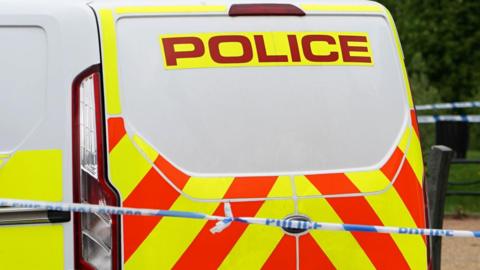 Police generic image of a police van which is white with red and yellow markings. In front of the van is a blue and white tape with 'police' written on it. 